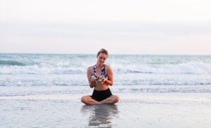 woman sits in shore of beach on sanibel holding shells